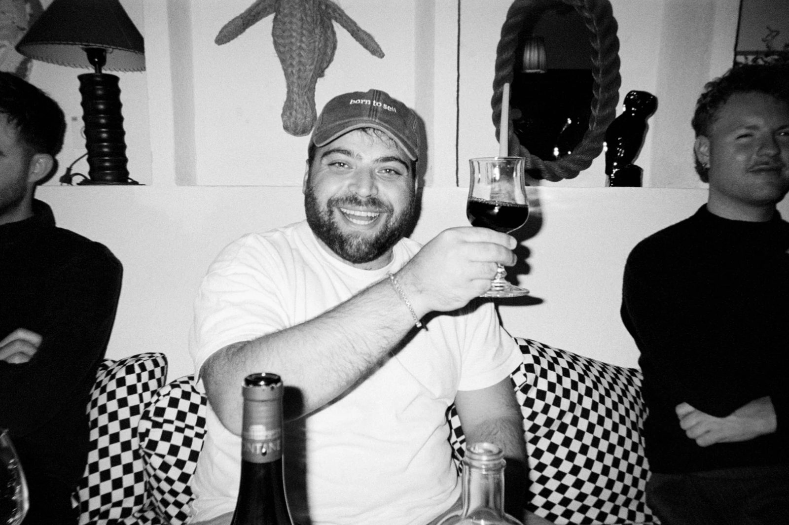 A Lighter in a born to sell cap raising a glass of red wine