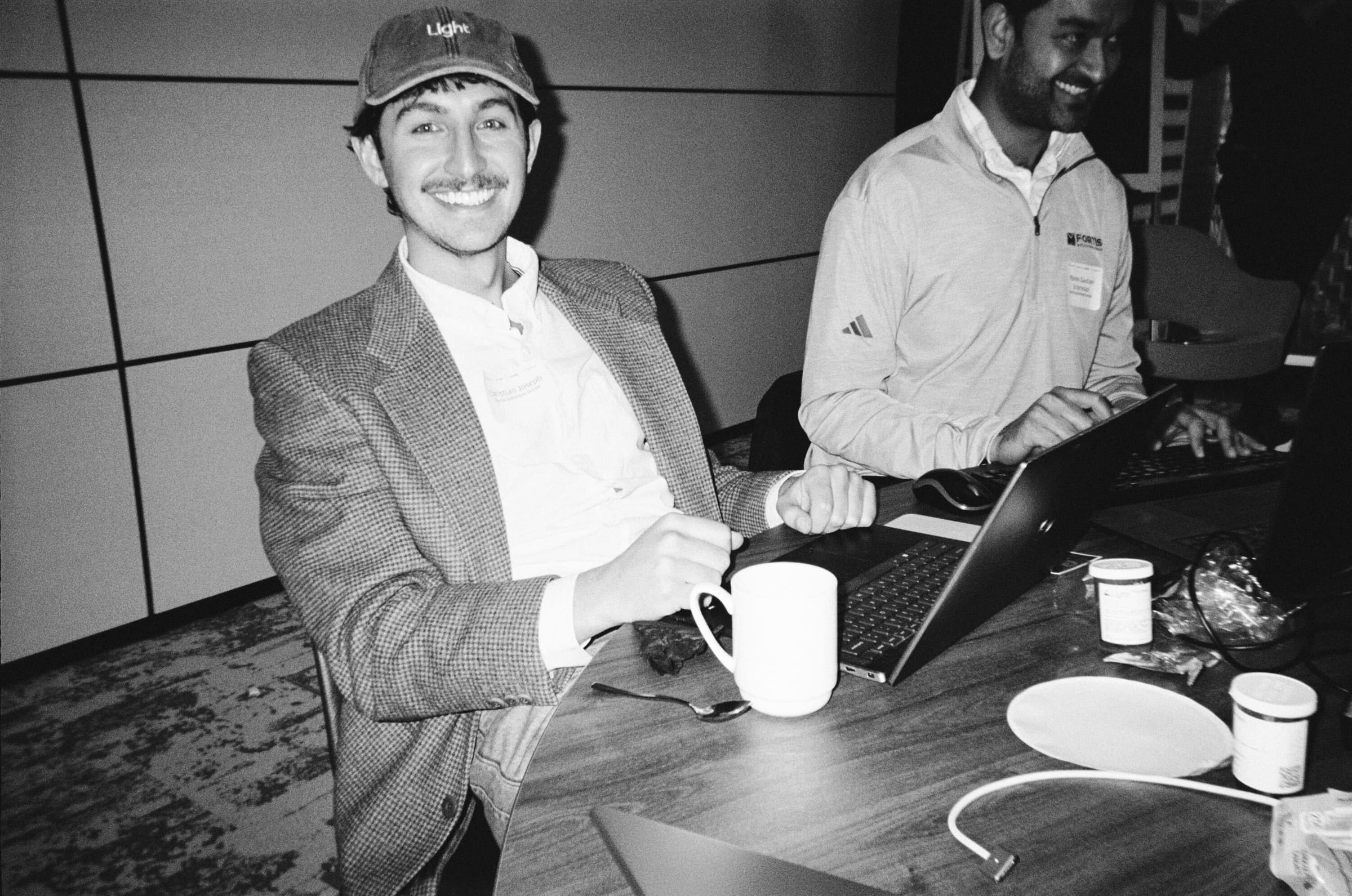 A smiling builder in a Light cap at a Light hackathon, laptop and coffee on the table