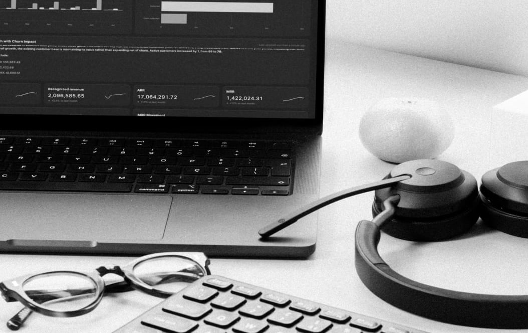 A laptop, headphones and reading glasses on a desk